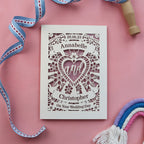 A luxury wedding card from the UK, laser cut and hand finished. Card has a heart in the centre and names in banners above and below. there is a date at the top and "on your wedding day" at the bottom