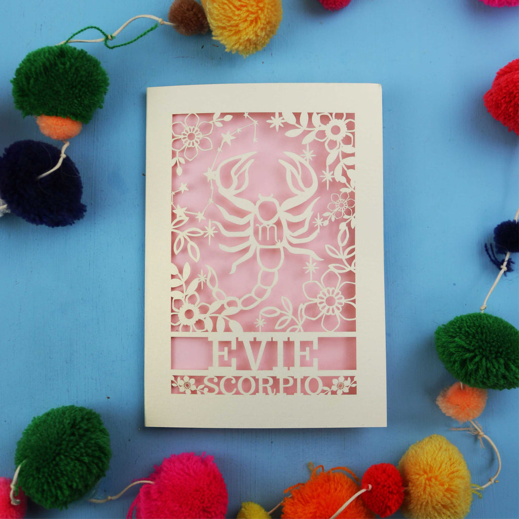Decorative Scorpio zodiac birthday card with 'Evie Scorpio' design on a blue background with colourful pom-poms.