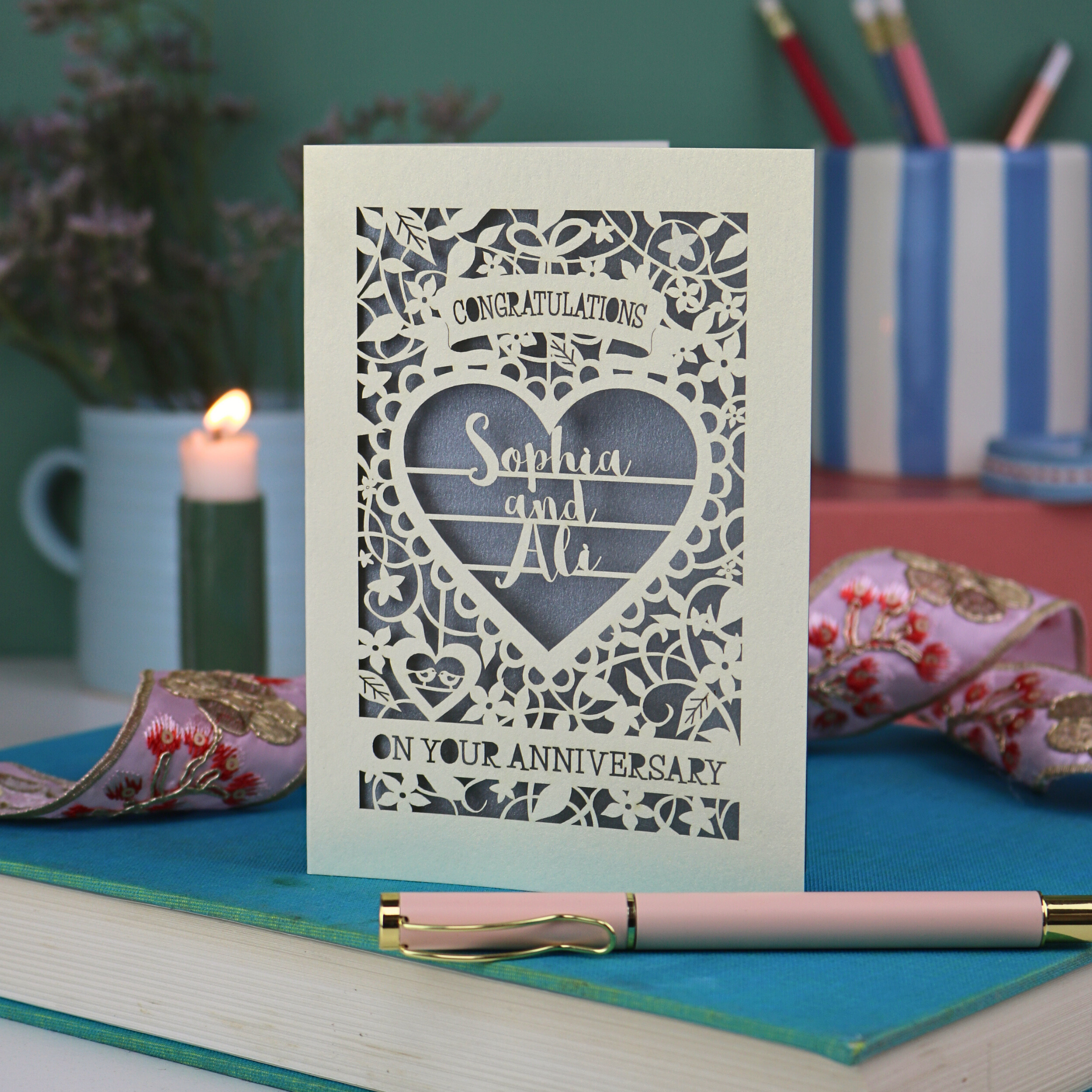 Personalised laser cut Anniversary card with decorative heart design on a book with a pen and candles in the background.