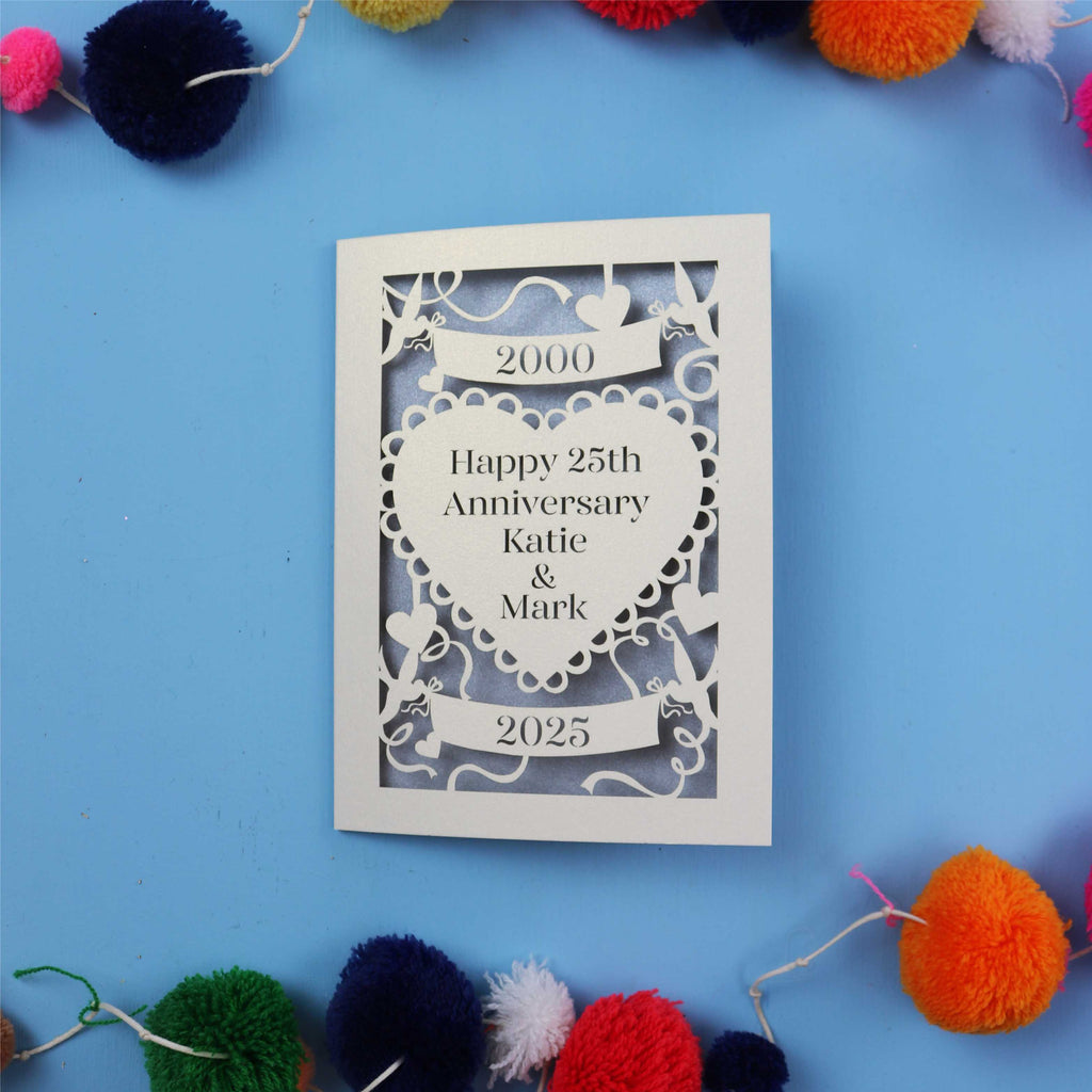 Decorative 25th anniversary card with cut-out design on a blue background with colourful pom-poms.