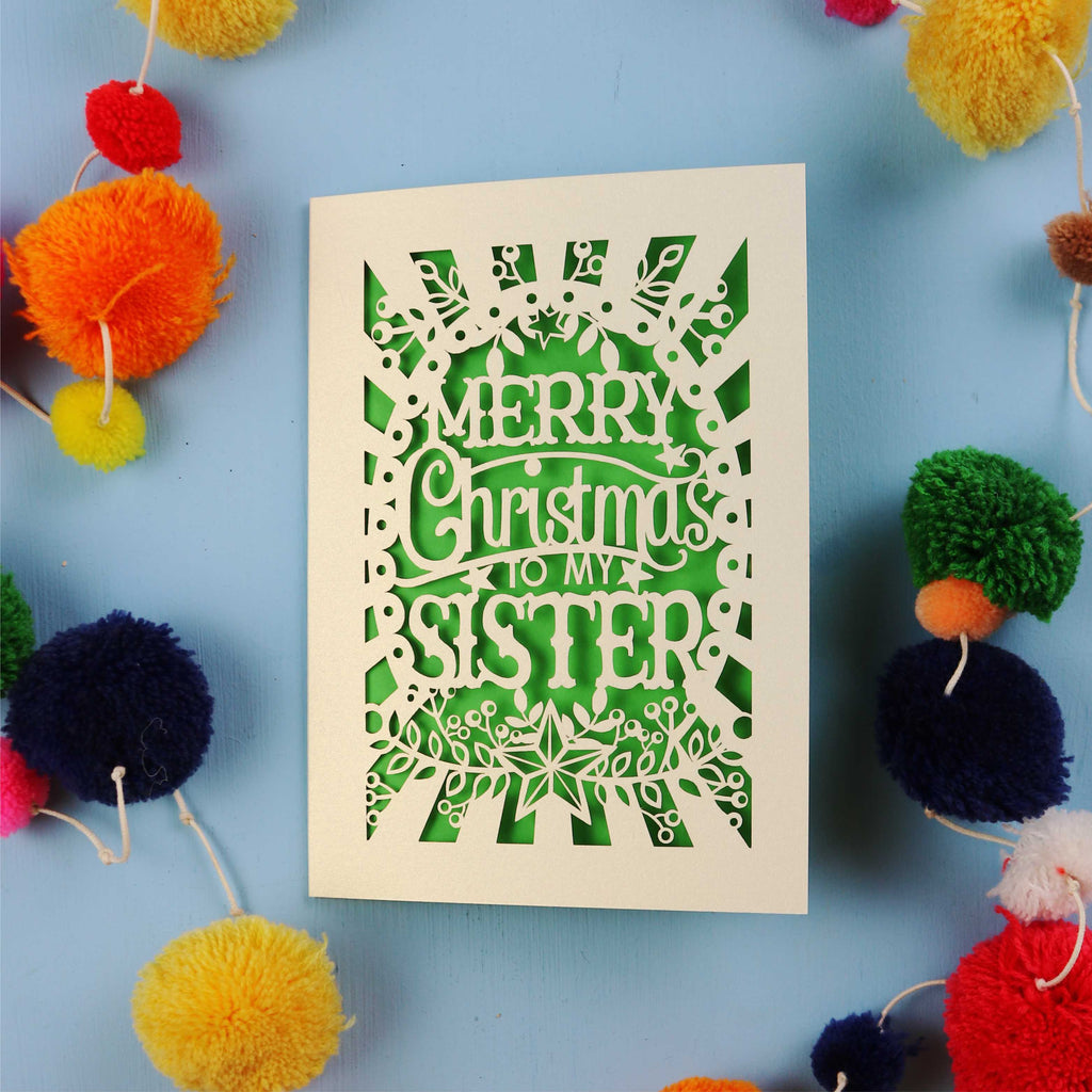 Sister Christmas card with 'Merry Christmas to my sister' text on a blue background with colourful pom-poms.