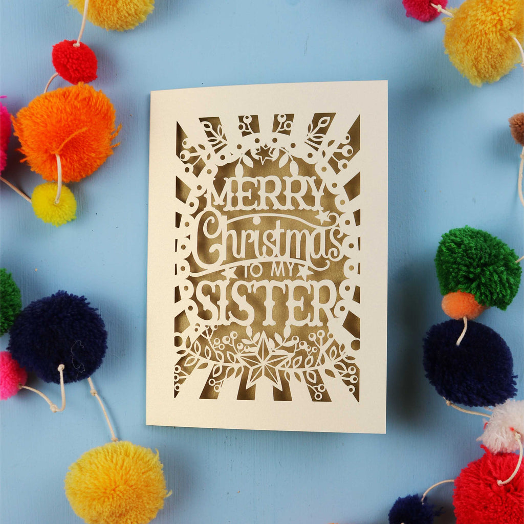 Sister Christmas card with 'Merry Christmas to my sister' text on a blue background with colourful pom-poms.
