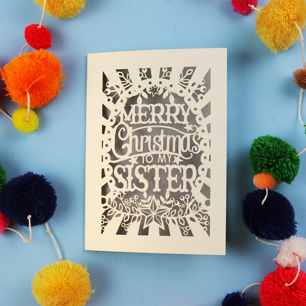 Sister Christmas card with 'Merry Christmas to my sister' text on a blue background with colourful pom-poms.