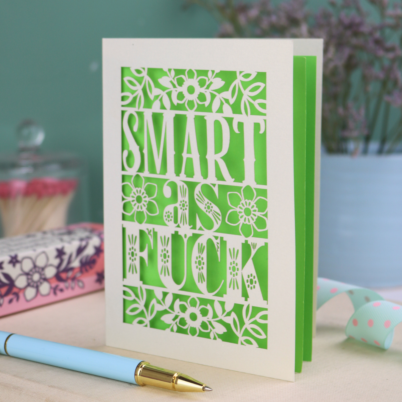 Card with 'Smart as F*ck' text on a desk with stationery items