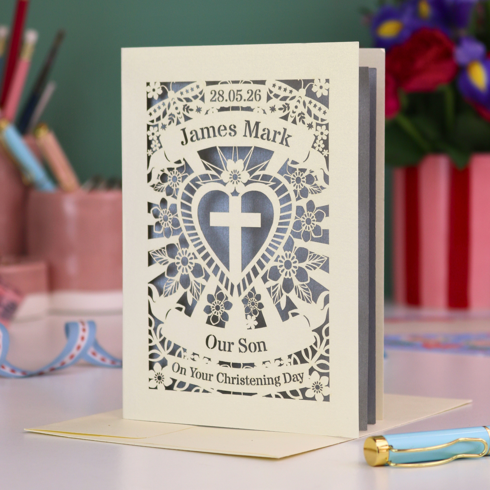 Personalized christening card with decorative design and text on a table with stationery items.
