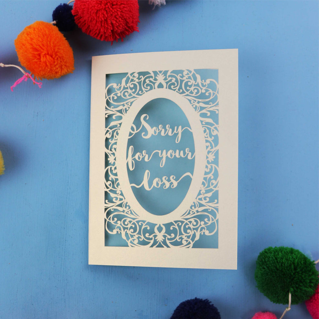 Beautiful Sympathy Card with 'Sorry for your loss' text laser cut from cream card with a light blue paper backing, on a blue background.