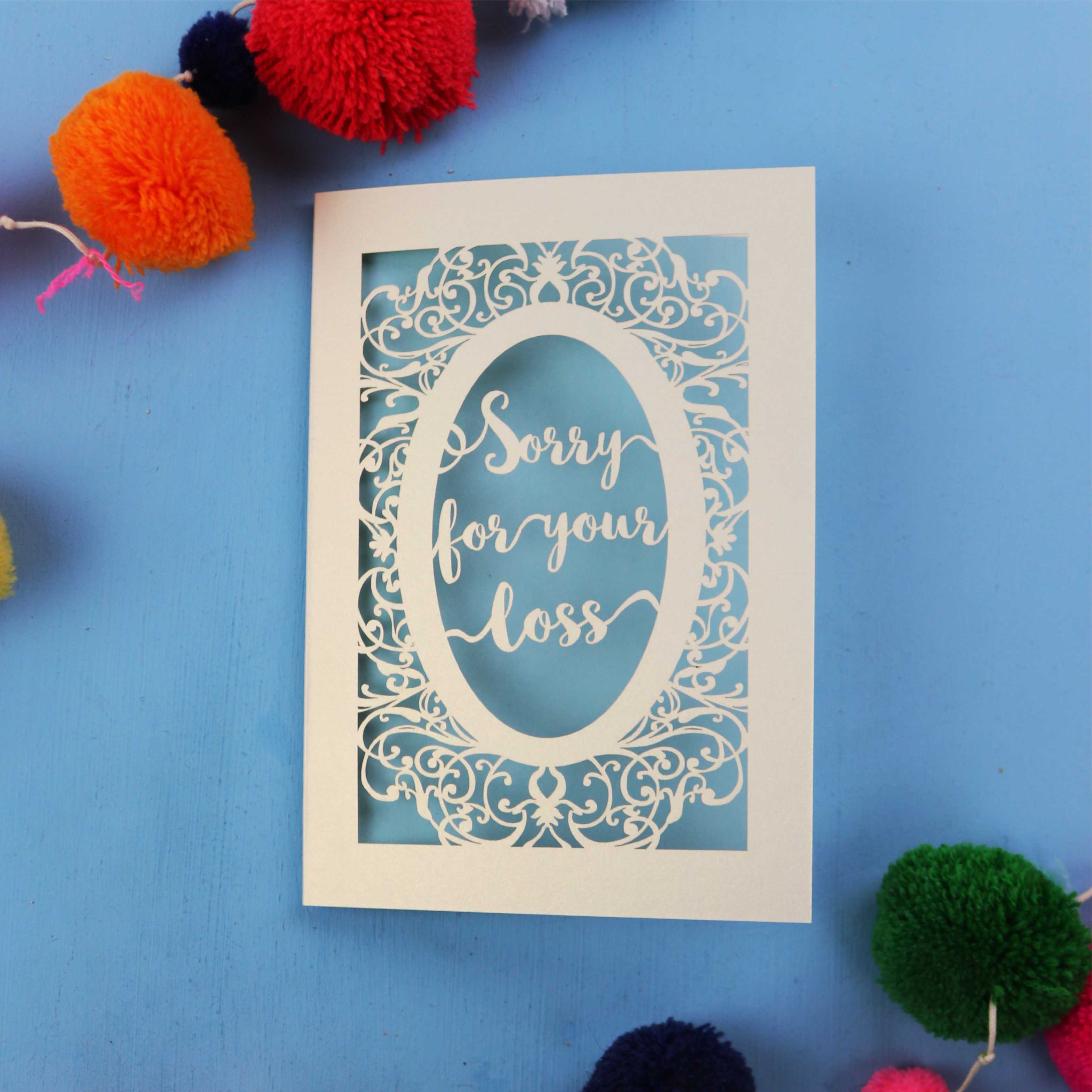 Beautiful Sympathy Card with 'Sorry for your loss' text laser cut from cream card with a light blue paper backing, on a blue background.