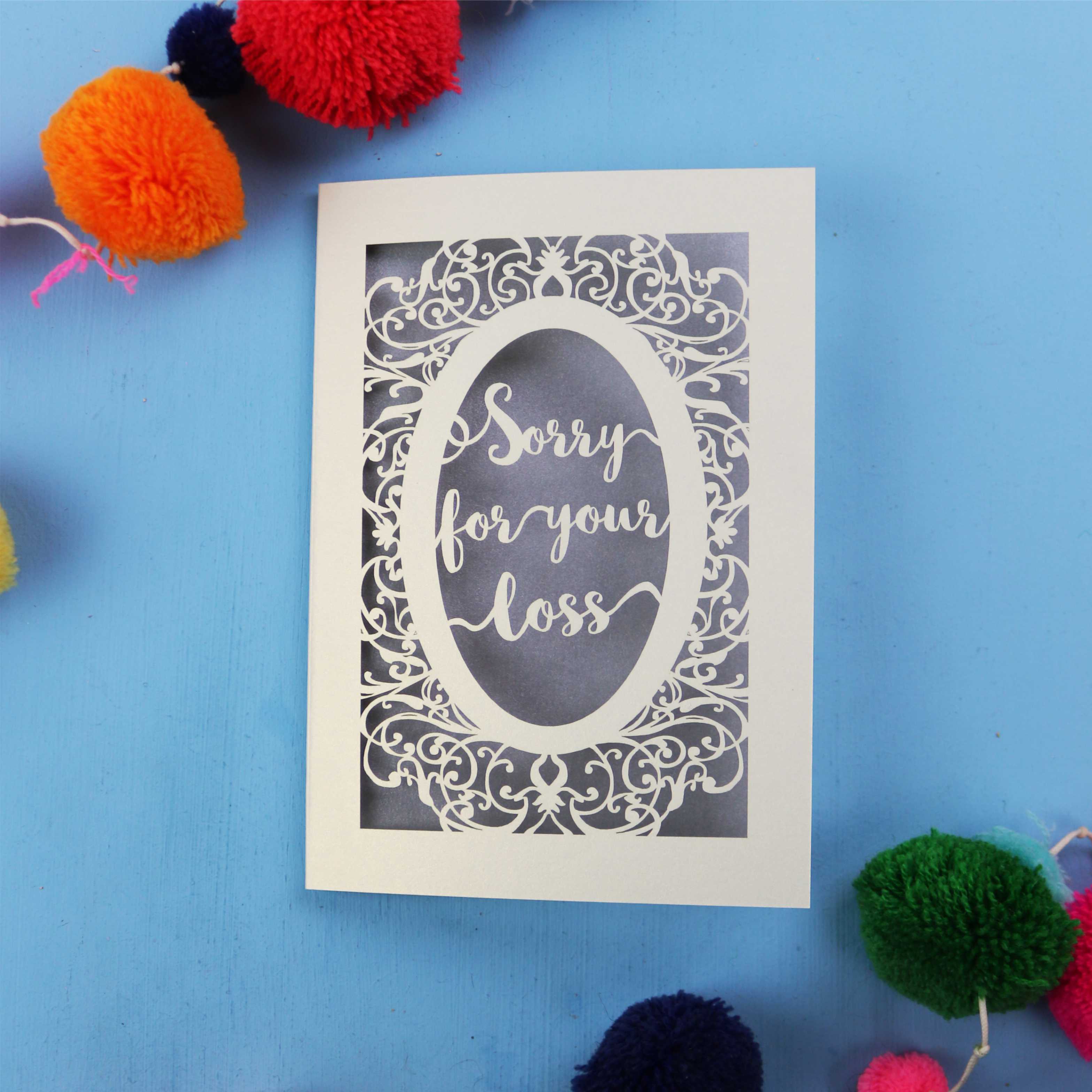 Luxury Sympathy Card with 'Sorry for your loss' text laser cut from cream card with a silver paper backing, on a blue background.