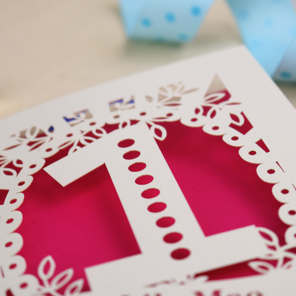 A cream laser cut 1st birthday card with floral border, a spotty number '1', and personalised with the name "Lily Mae" in a stencil font cut out lettering.