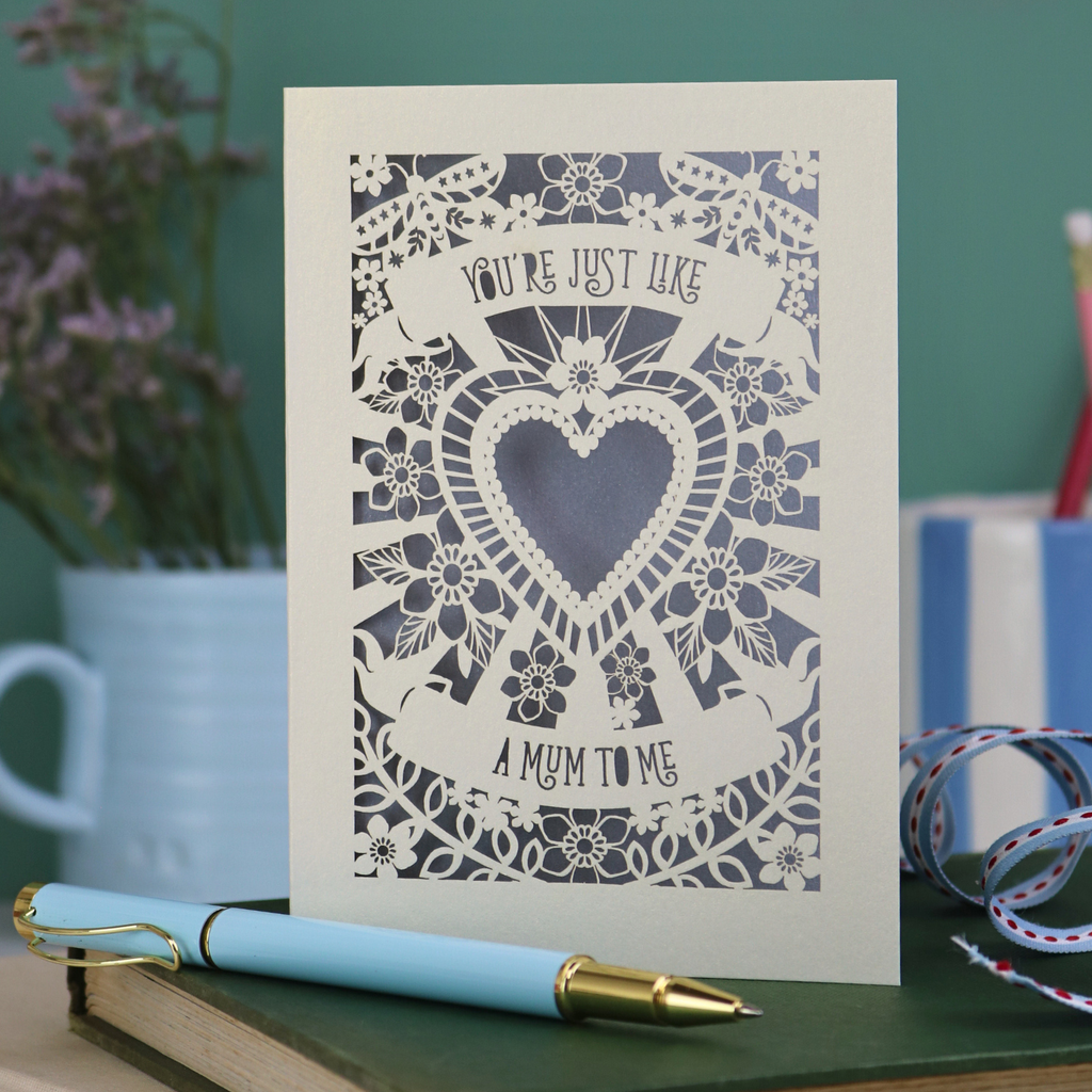 Decorative Step-mum Mother's Day card with floral design and text 'You're just like a mum to me' on a green surface with a pen and mug in the background.