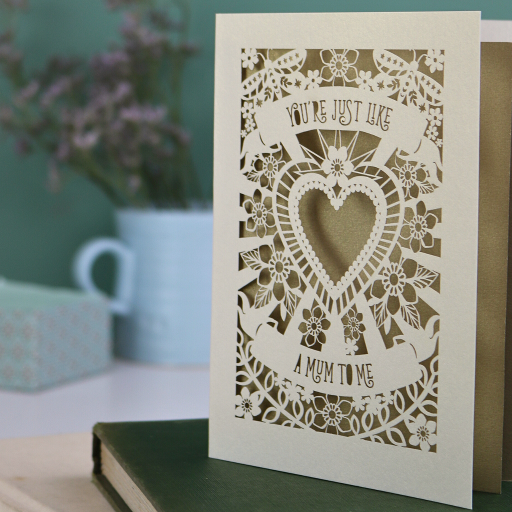 Decorative Step-mum Mother's Day card with floral design and text 'You're just like a mum to me' on a green surface with a pen and mug in the background.