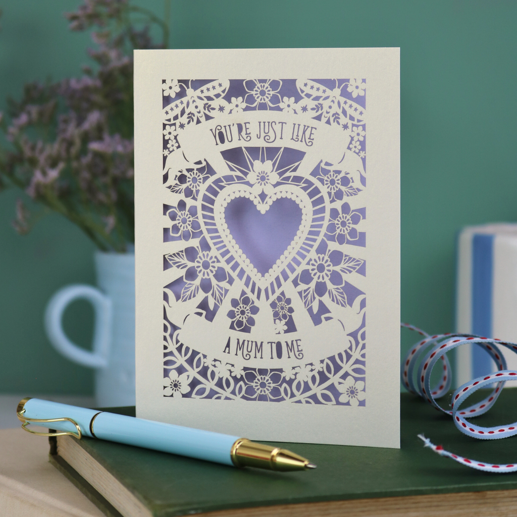 Decorative Step-mum Mother's Day card with floral design and text 'You're just like a mum to me' on a green surface with a pen and mug in the background.