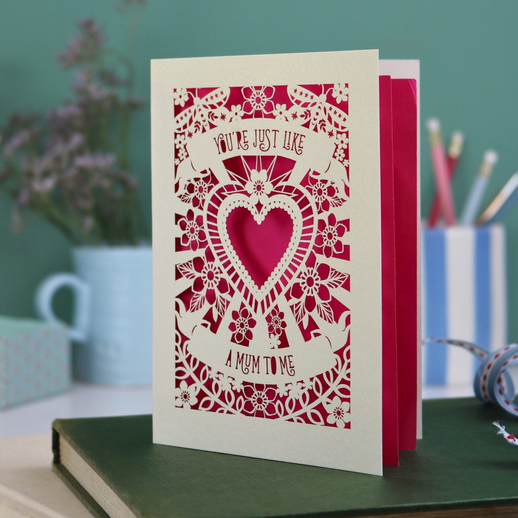 Decorative Step-mum Mother's Day card with floral design and text 'You're just like a mum to me' on a green surface with a pen and mug in the background.