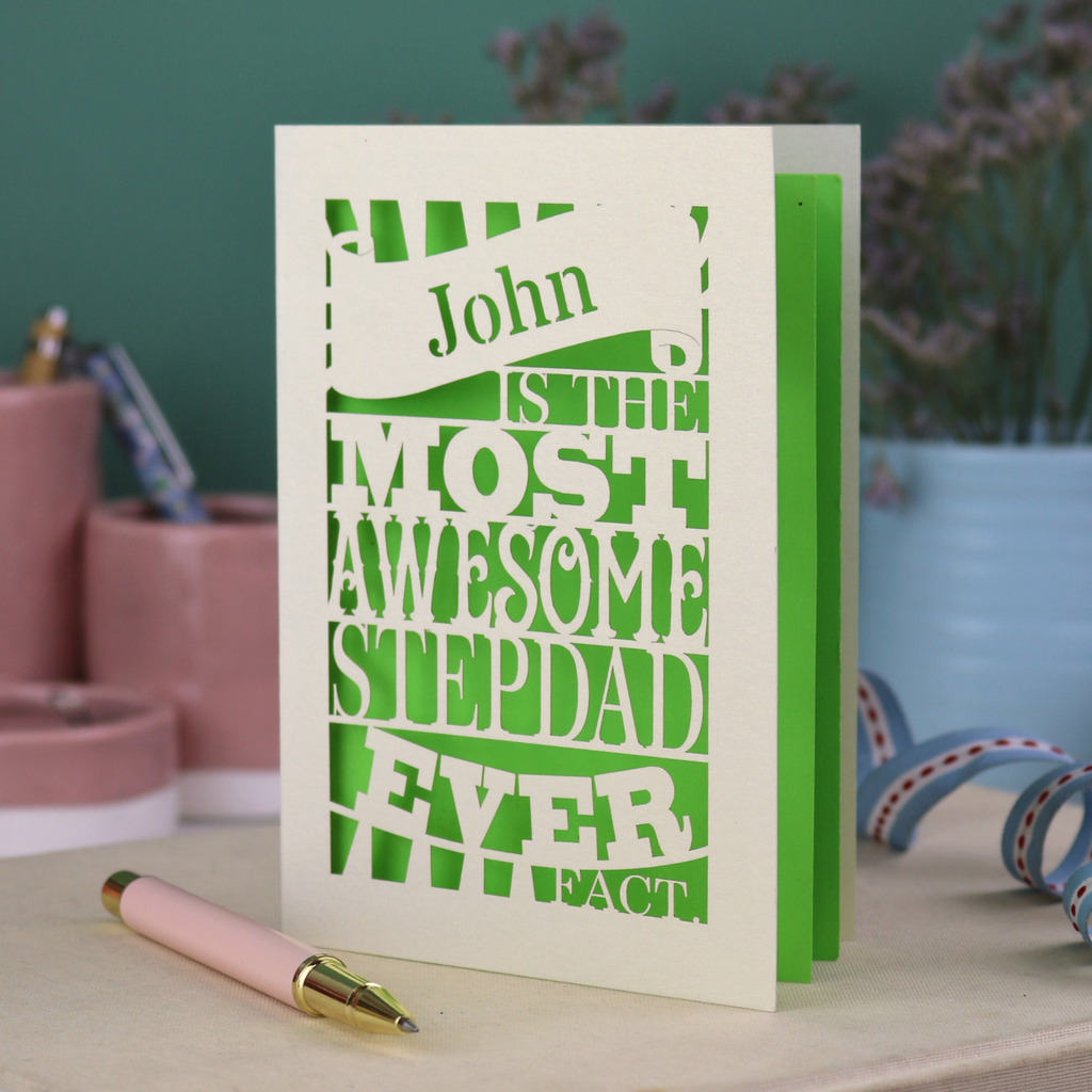 Laser cut Step dad Father's day Card with personalized text, "John is the most awesome stepdad ever. Fact." on a table with decorative items