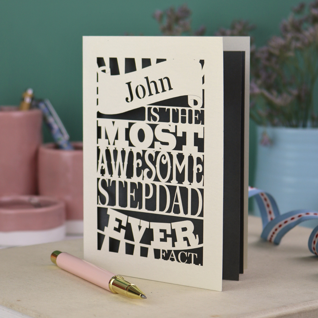 Paper cut Stepdad Father's day Card with personalized text, "John is the most awesome stepdad ever. Fact." on a table with decorative items