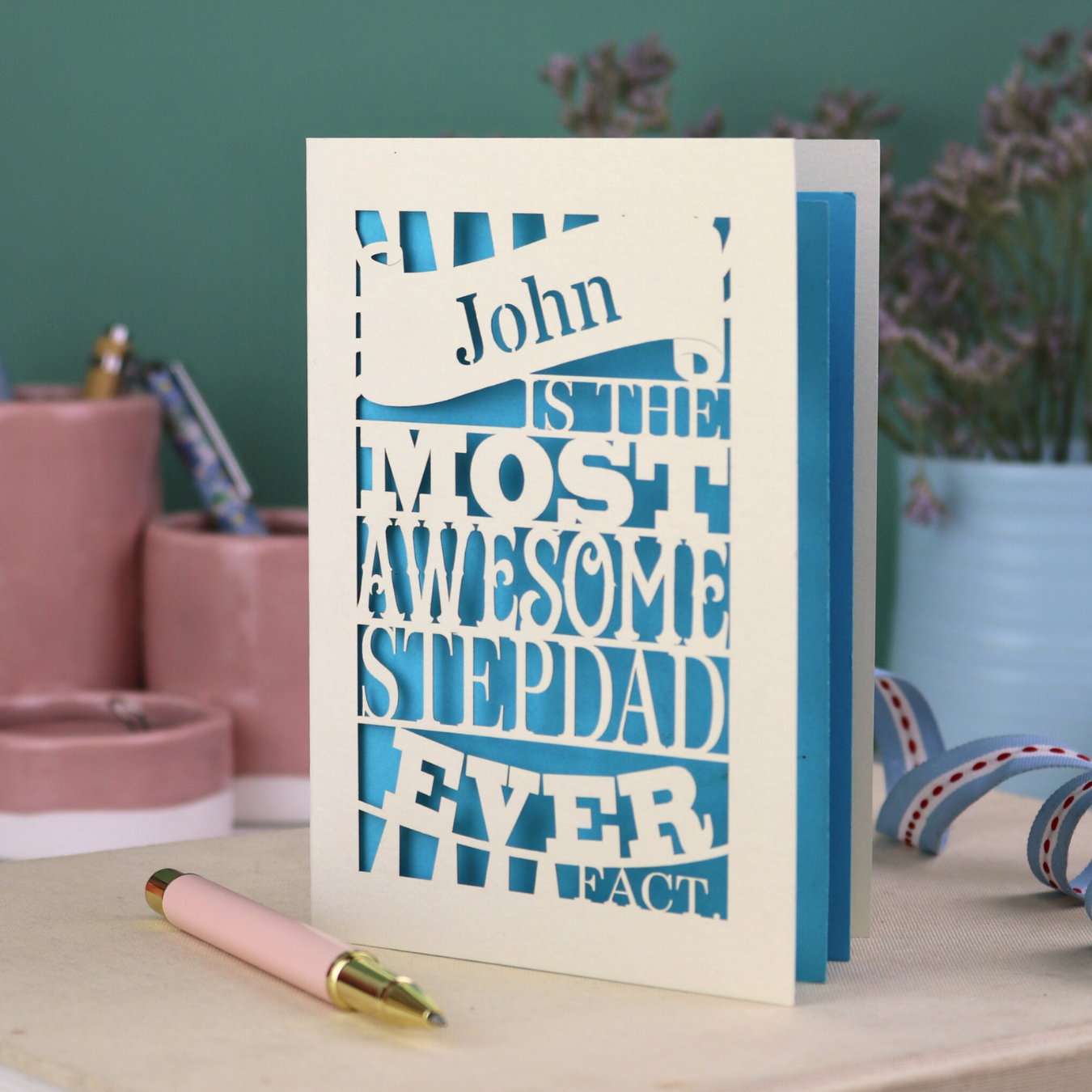 Laser cut Stepdad Father's day Card with personalized text, "John is the most awesome stepdad ever. Fact." on a table with decorative items