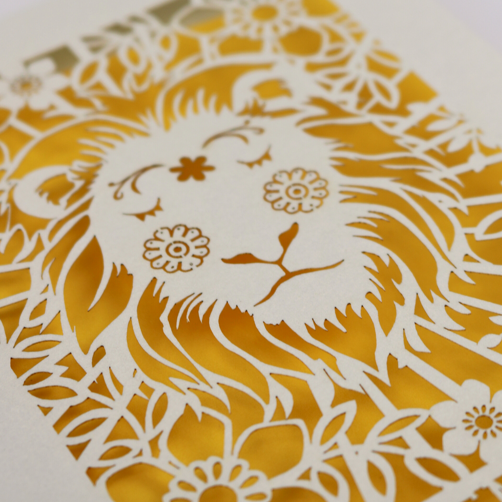 A close up detail of a laser cut greetings card based on the Strength tarot card, with cut out lion design and the word "Strength" 