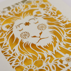 A close up detail of a laser cut greetings card based on the Strength tarot card, with cut out lion design and the word "Strength" 