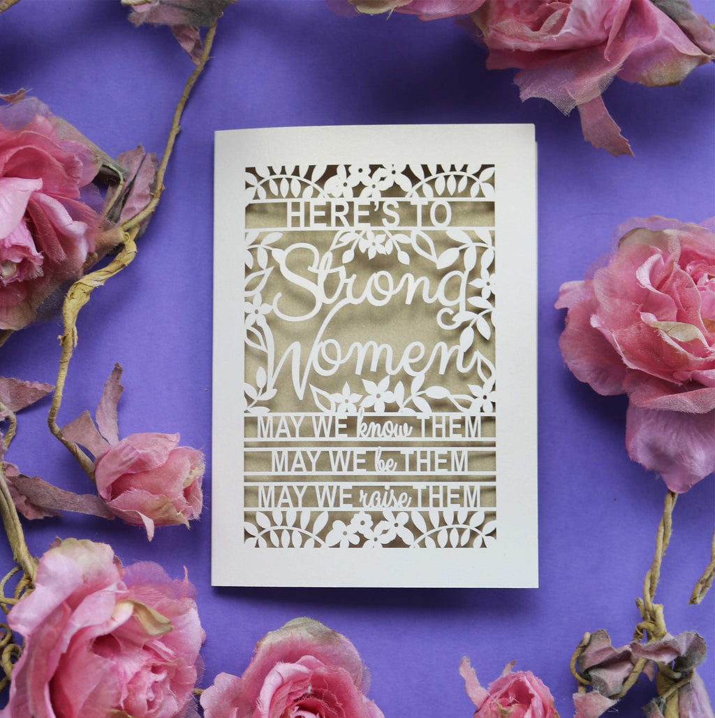A laser cut strong girl's Card that says "Here's to Strong Women, may we know them, may we be them, may we raise them"
