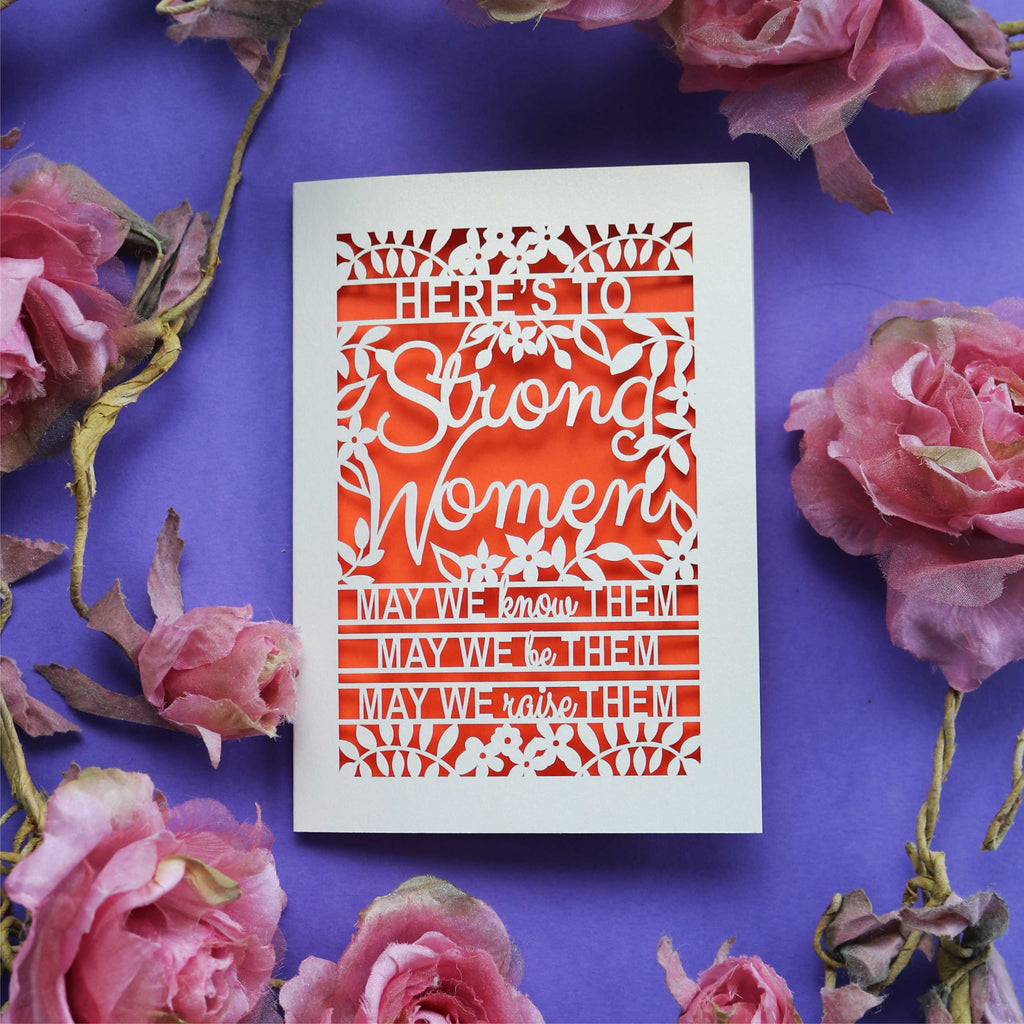 A laser cut International Women's Day Card that says "Here's to Strong Women, may we know them, may we be them, may we raise them"