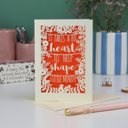 A handmade thank you teacher card with decorative text, 'It takes a big heart to help shape little minds' and floral patterns on a desk with stationery items.