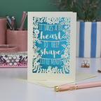A keepsake thank you teacher card with decorative text, 'It takes a big heart to help shape little minds' and floral patterns on a desk with stationery items.