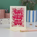A papercut thank you teacher card with decorative text, 'It takes a big heart to help shape little minds' and floral patterns on a desk with stationery items.