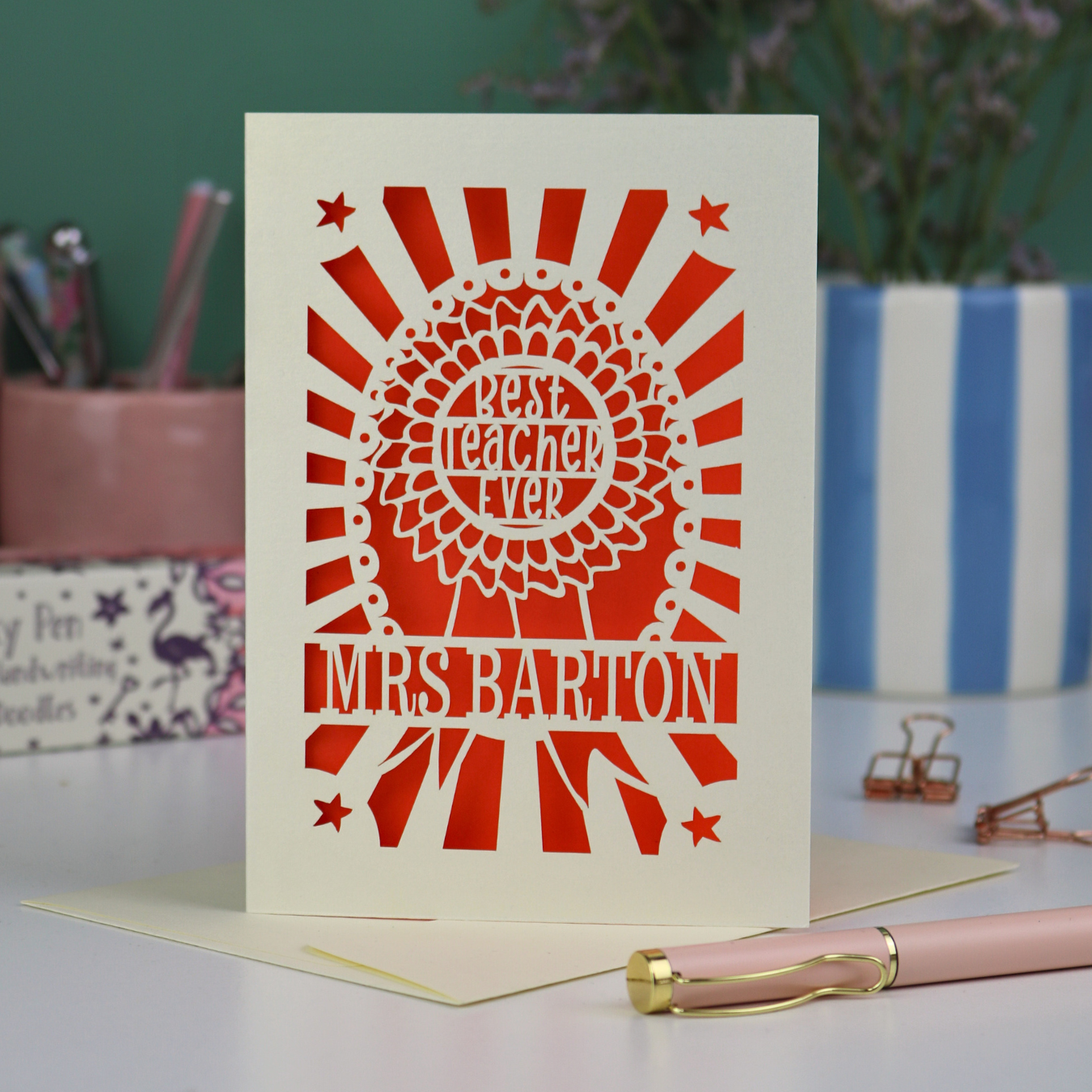 A personalised thank you teacher card with rosette design and the words "Best teacher ever" in the centre of the rosette, personalised with the teacher's name underneath. Card is laser cut cream with an orange paper insert