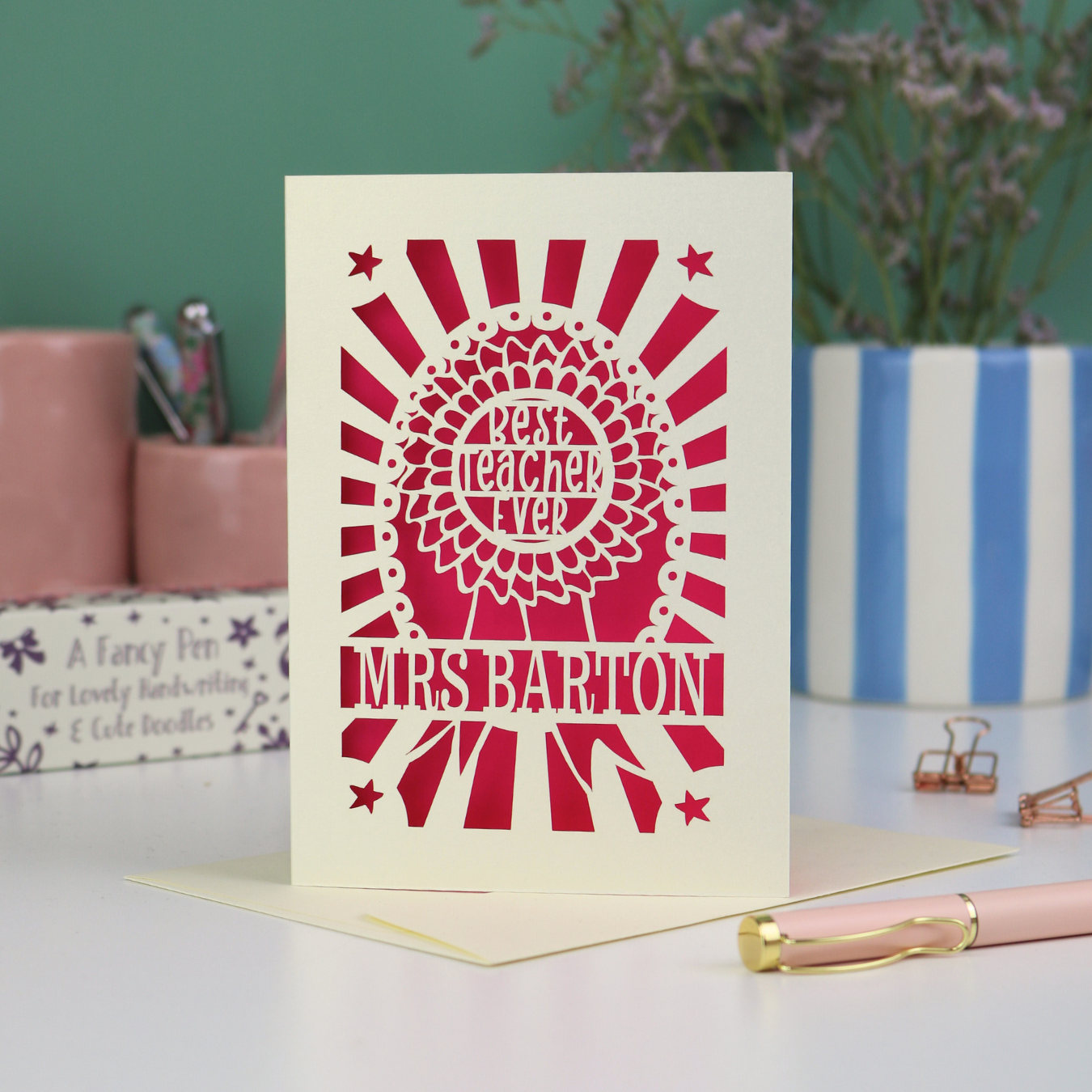 A laser cut thank you teacher card with rosette design and the words "Best teacher ever" in the centre of the rosette, personalised with the teacher's name underneath. Card is cream with a bright pink paper insert