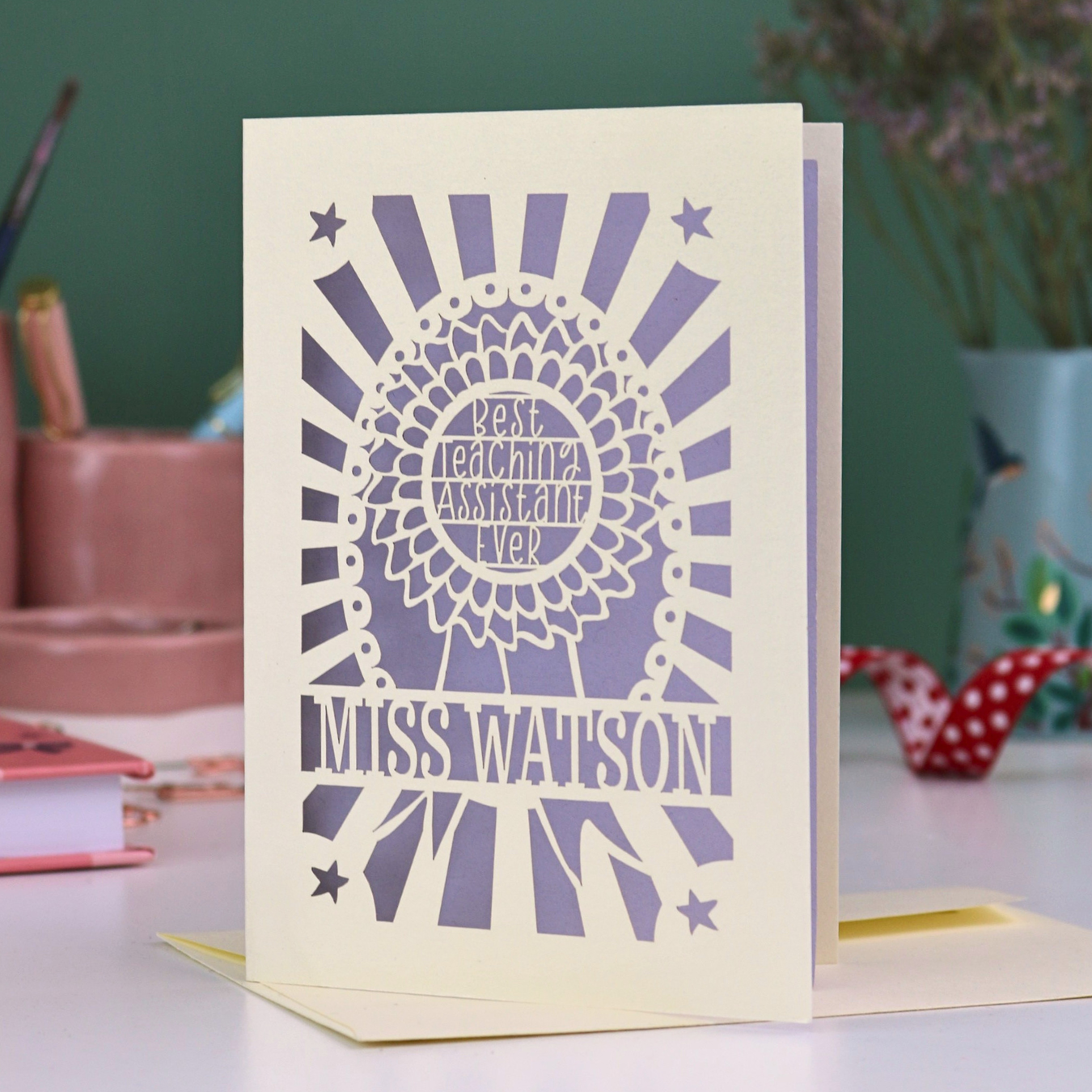 A personalised thank you teaching assistant card with cut out rosette design and text "Best Teaching Assistant Ever" and personalised with the name "Miss Watson"