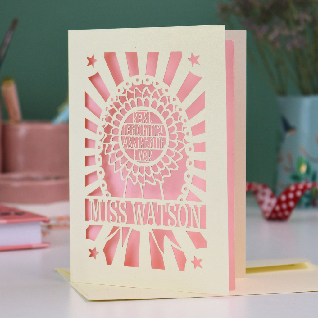 A laser cut thank you teaching assistant card with cut out rosette design and text "Best Teaching Assistant Ever" and personalised with the name "Miss Watson" in cream and candy pink