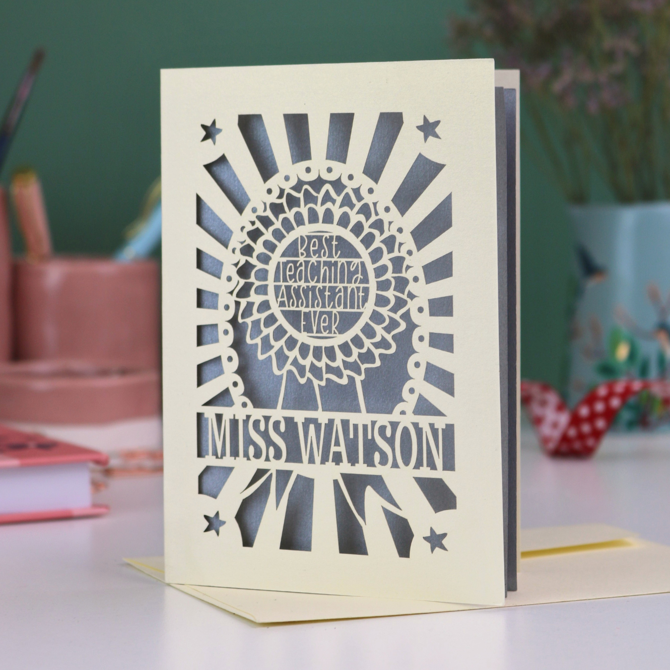A laser cut thank you teaching assistant card with cut out rosette design and text "Best Teaching Assistant Ever" and personalised with the name "Miss Watson"