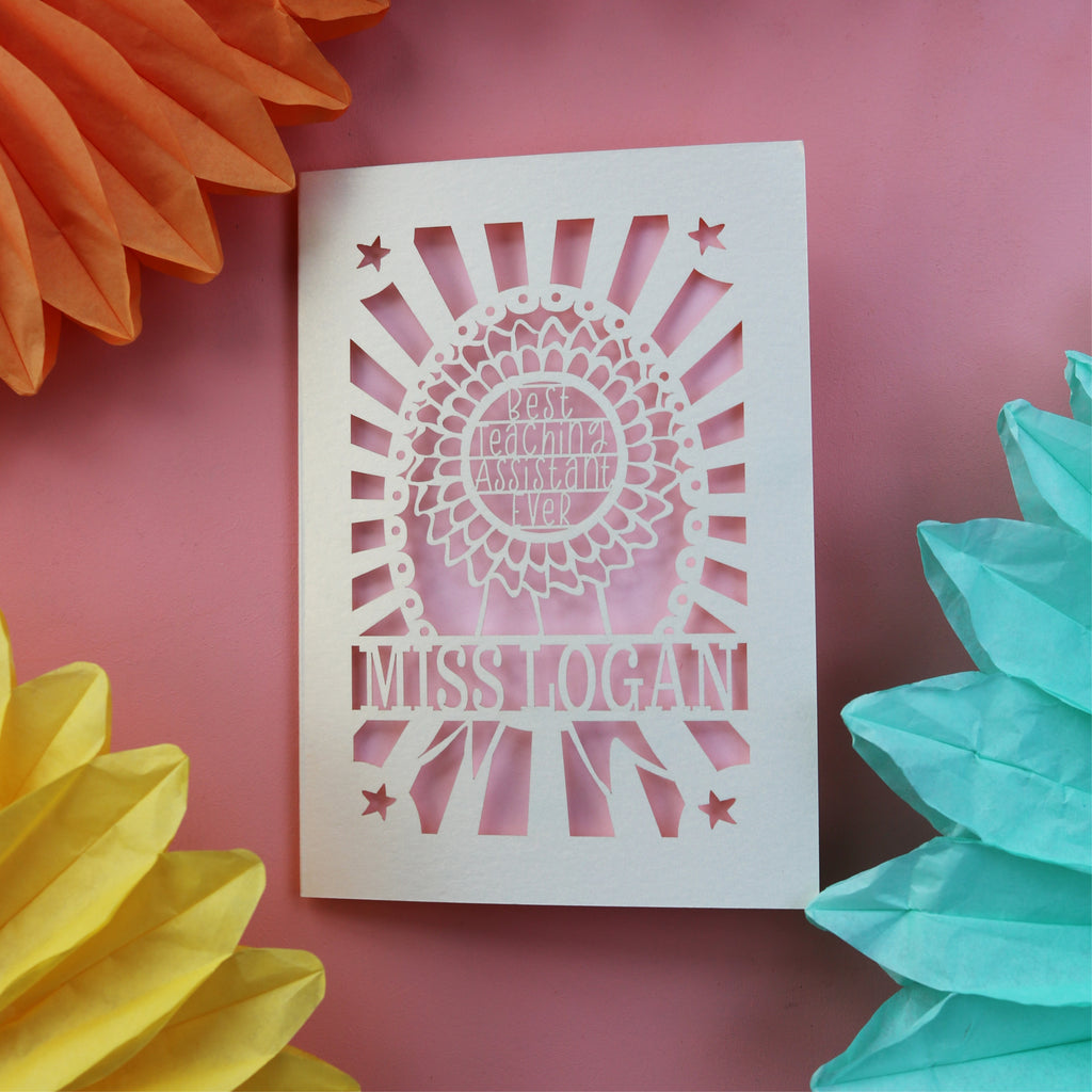 A personalised thank you teacher card for a teaching assistant. Card has a rosette with "Best teaching assistant ever" and is personalised with their name