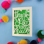 Laser cut thank you card with 'Thank you so very much' text on a blue background with colourful pom-poms.