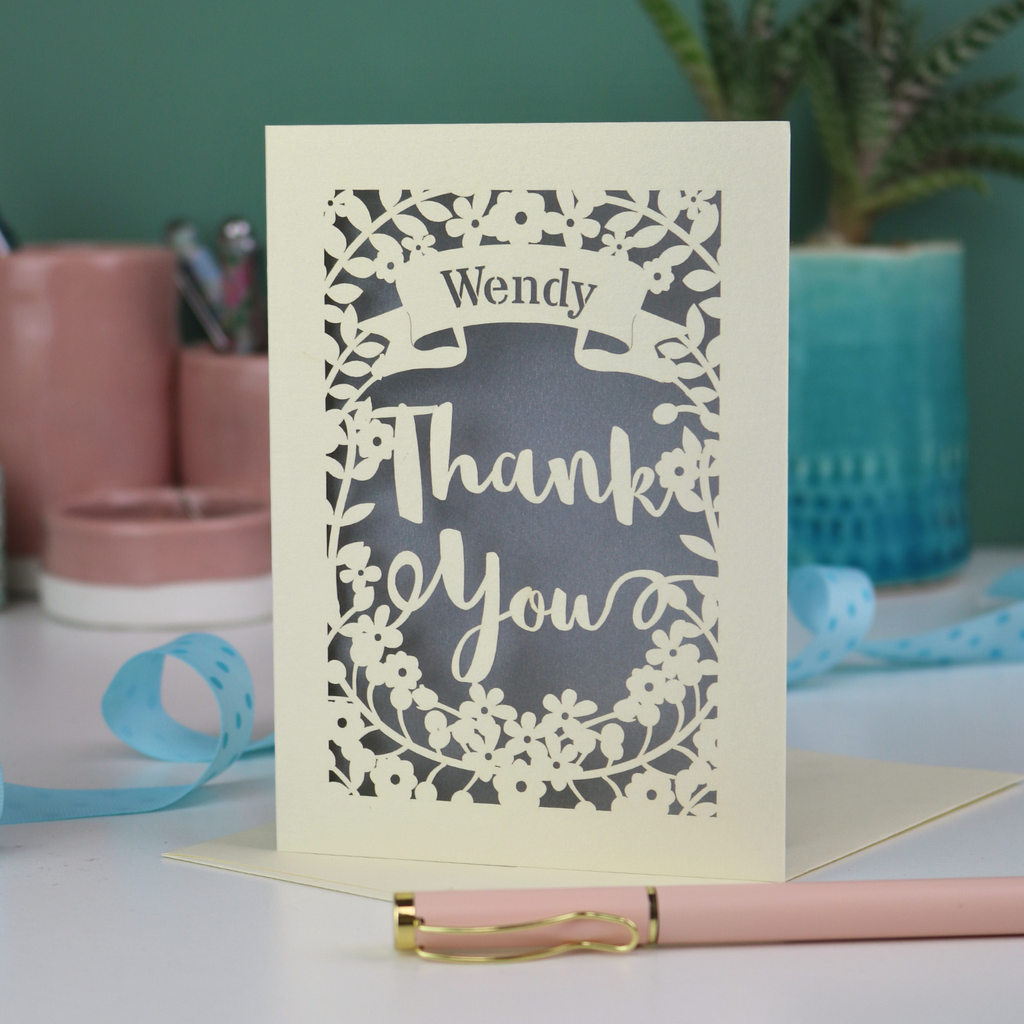 Laser cut Thanks card with decorative border on a desk with stationery items.