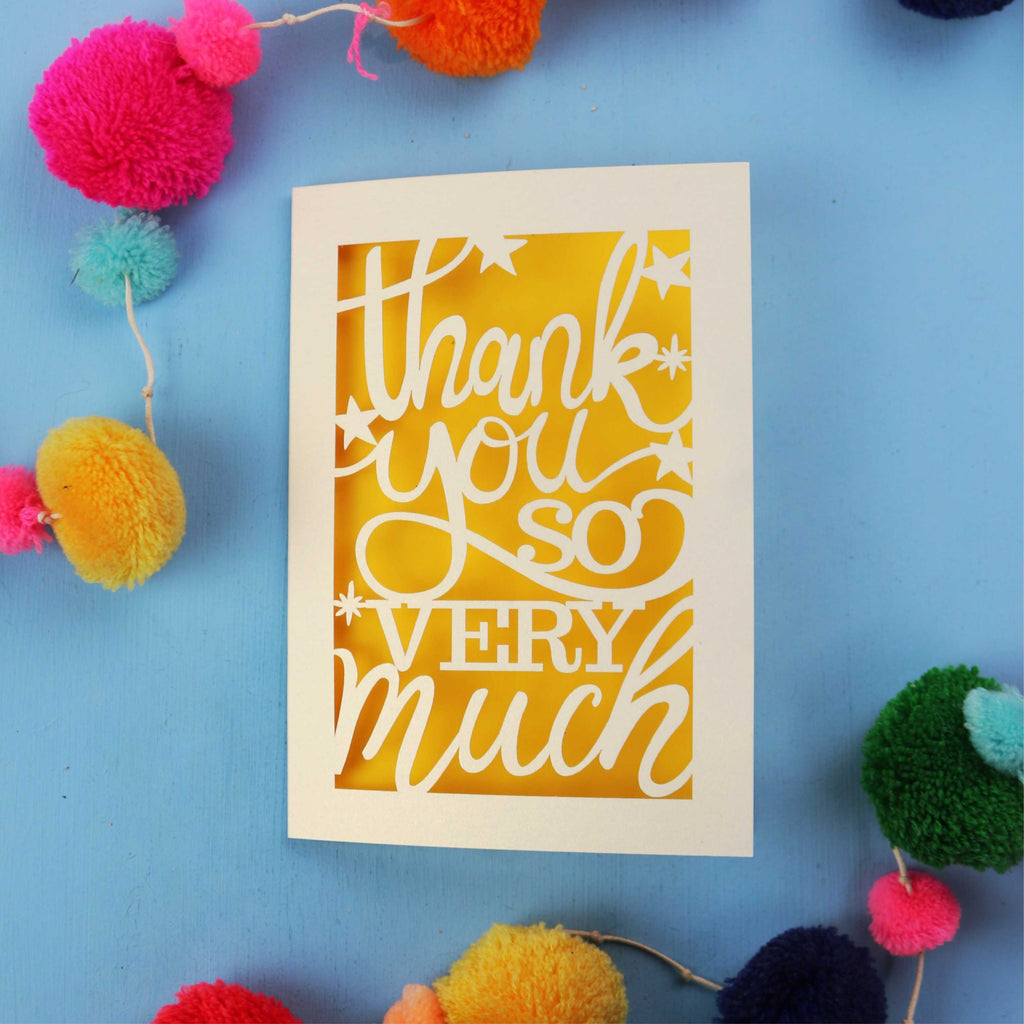 Laser cut thank you card with 'Thank you so very much' text on a blue background with colourful pom-poms.