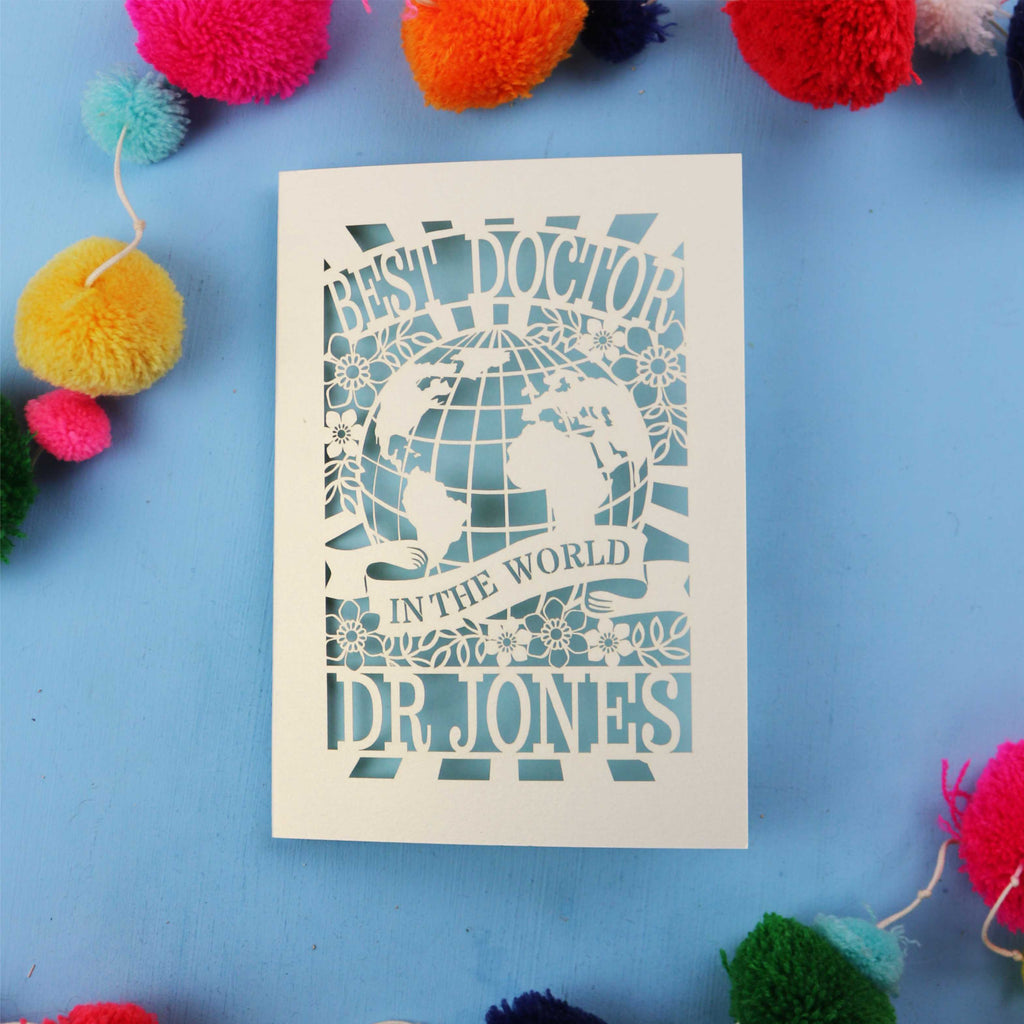 Personalised thank you Doctor card with 'Best Doctor in the World' text on a blue background with colourful pom-poms.