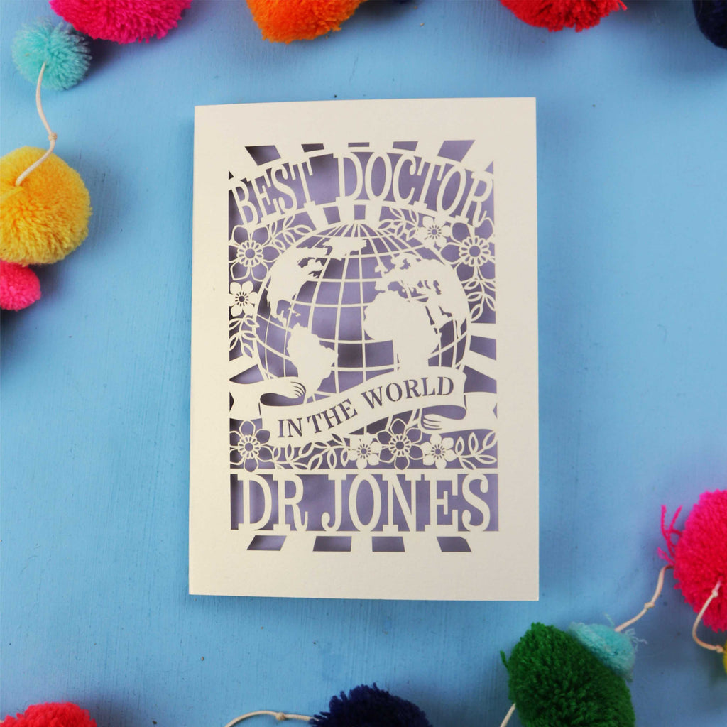 Personalised thanks Doctor card with 'Best Doctor in the World' text on a blue background with colourful pom-poms.
