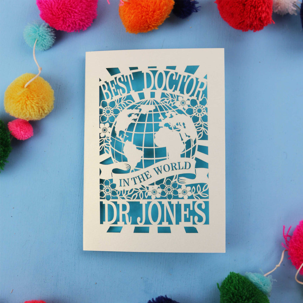 Personalised thank you Doctor card with 'Best Doctor in the World' text on a blue background with colourful pom-poms.