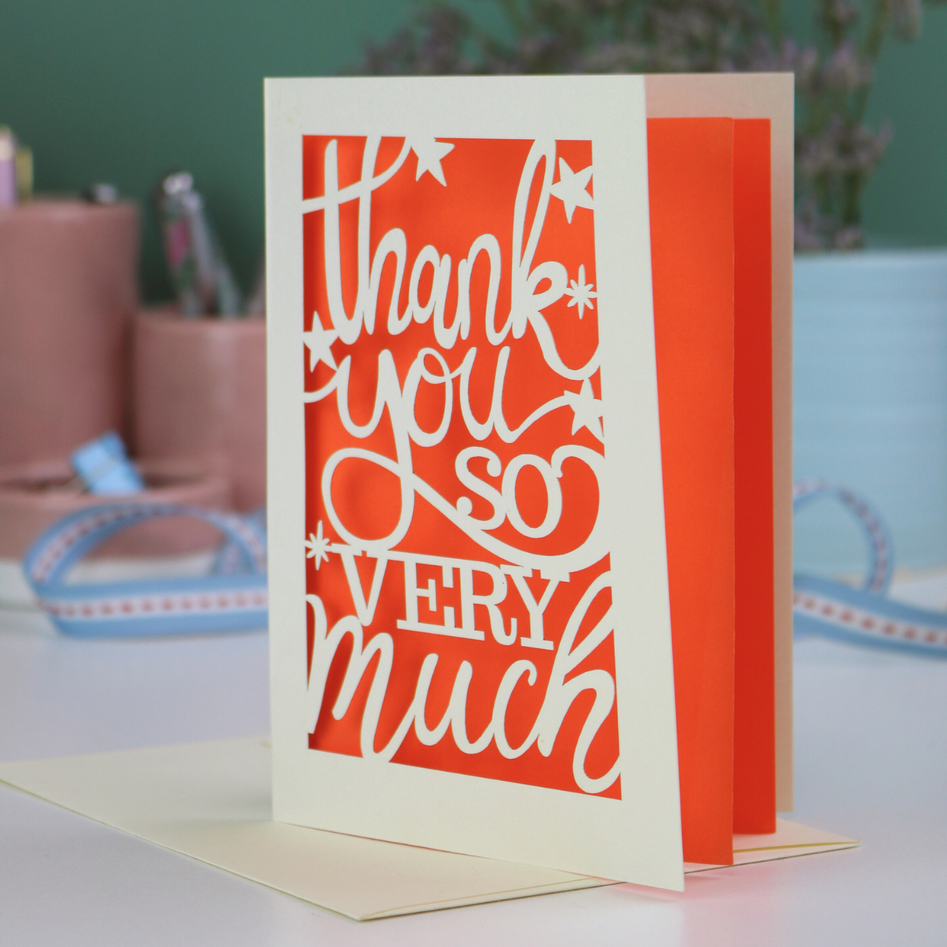A laser cut Thank You card with handwritten cut out text that says "Thank you so very much", with an orange paper insert. 