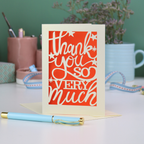A laser cut Thank You card with handwritten cut out text that says "Thank you so very much", with an orange paper insert. 
