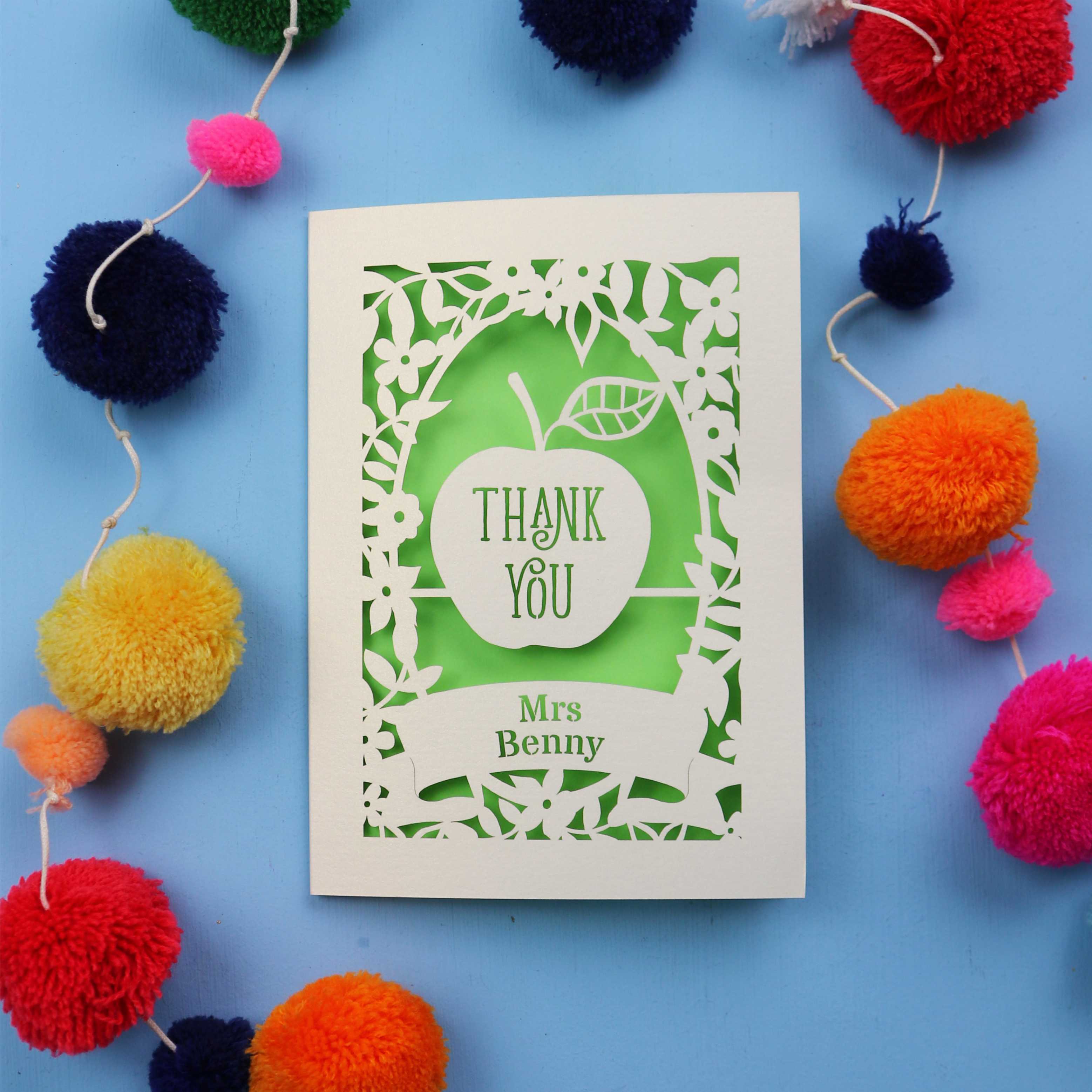 Personalised thank you teacher card with 'Thank You Mrs Benny' text surrounded by colourful pom-poms on a blue background