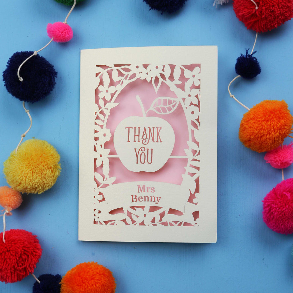 Personalised laser cut thank you teacher card with 'Thank You Mrs Benny' text surrounded by colourful pom-poms on a blue background