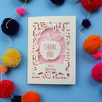 Personalised laser cut thank you teacher card with 'Thank You Mrs Benny' text surrounded by colourful pom-poms on a blue background