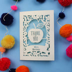 Personalised teacher card with 'Thank You Mrs Benny' text surrounded by colourful pom-poms on a blue background