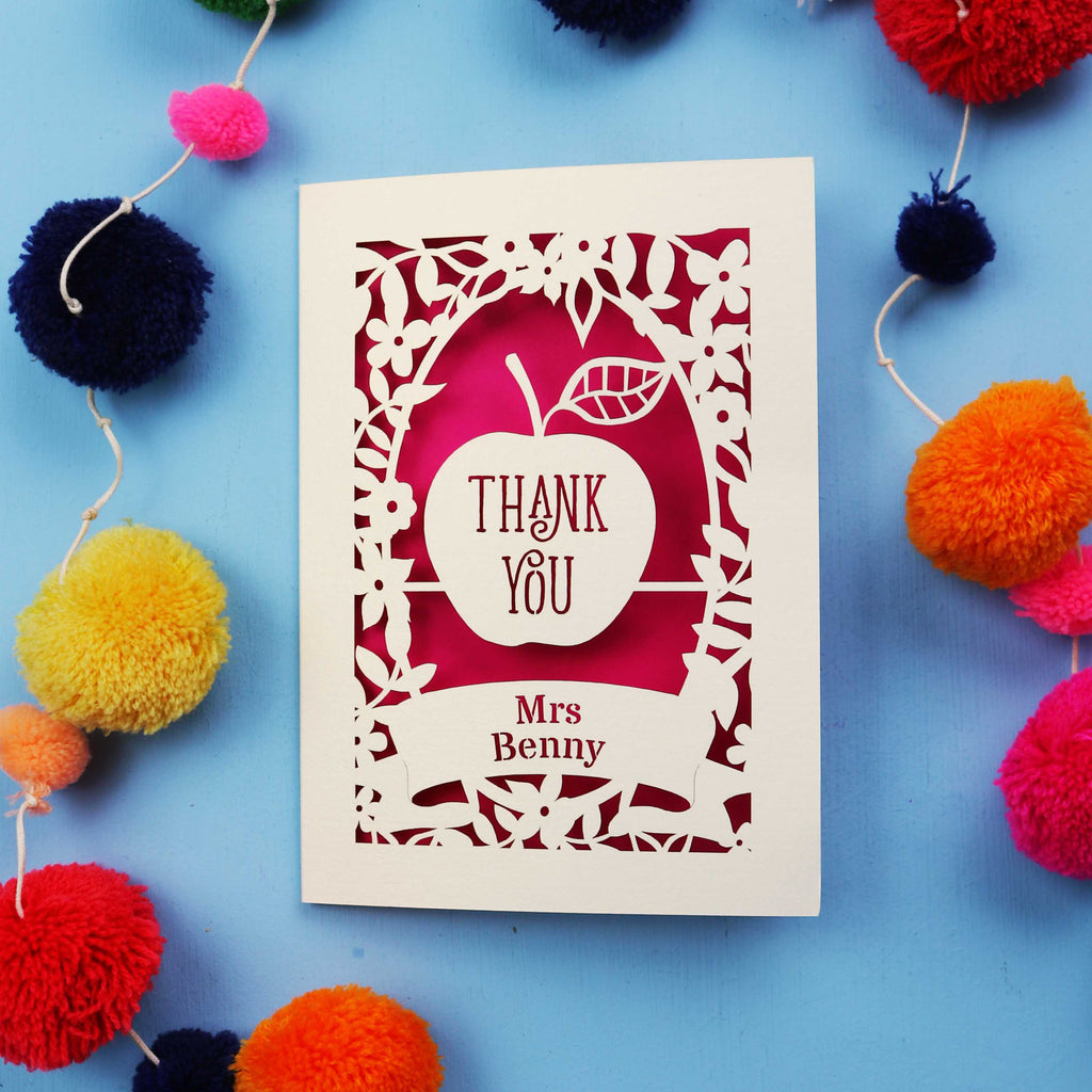 Personalised cut out thank you teacher card with 'Thank You Mrs Benny' text surrounded by colourful pom-poms on a blue background