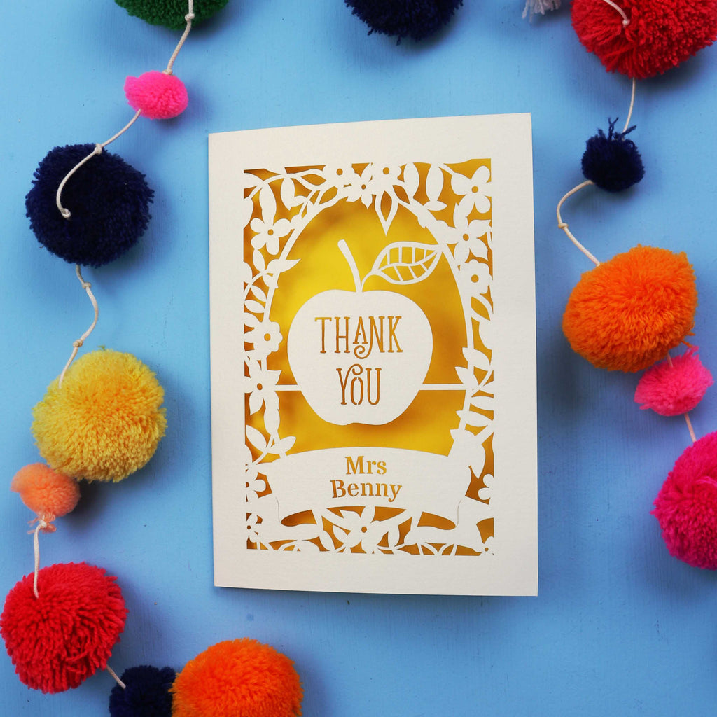 Personalised thank you teacher card with 'Thank You Mrs Benny' text surrounded by colourful pom-poms on a blue background