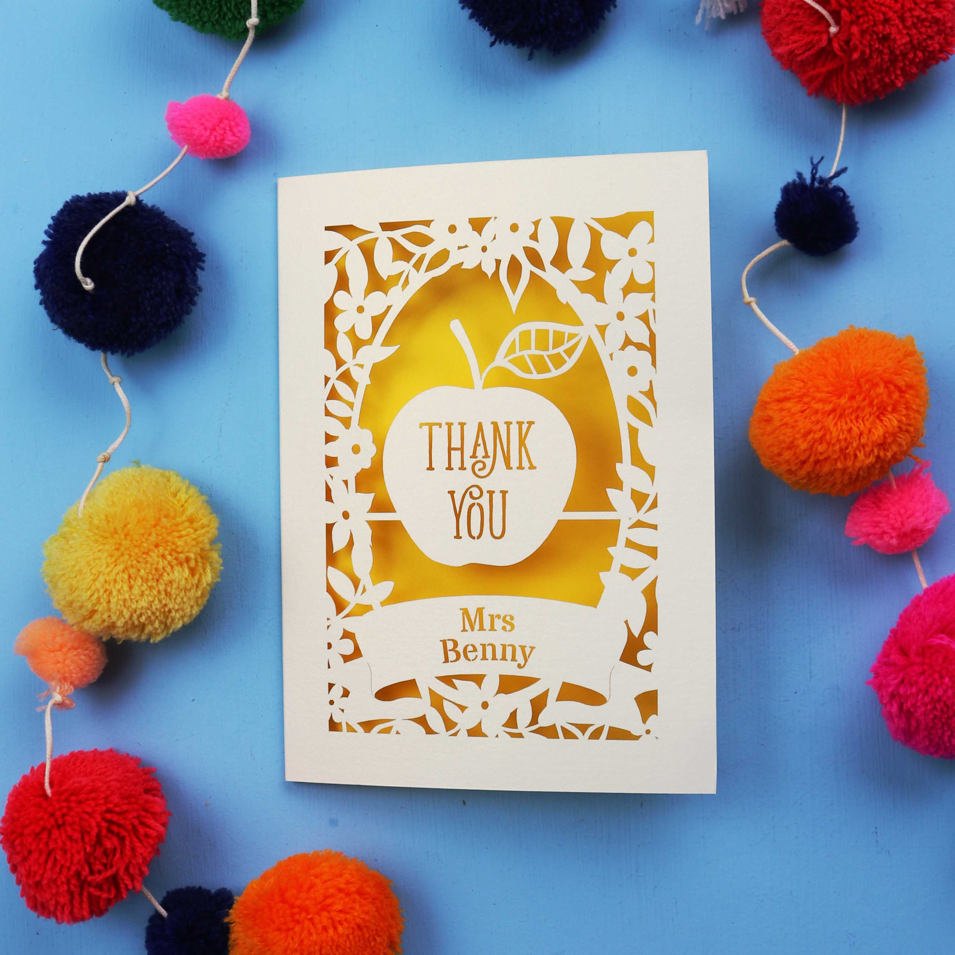 Personalised thank you teacher card with 'Thank You Mrs Benny' text surrounded by colourful pom-poms on a blue background