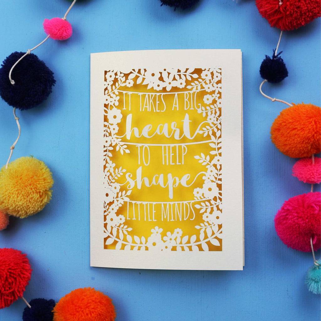 Laser cut Thank you teacher card with motivational quote surrounded by colourful pom-poms on a blue background