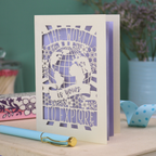 Greeting card with laser cut design and 'The world is yours to explore' text on a wooden surface.